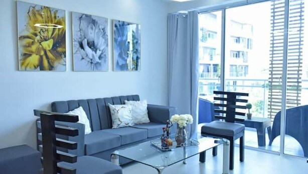 A modern living room with a grey sofa, a glass coffee table, and a view of a balcony with outdoor furniture.