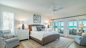 Ein Schlafzimmer mit einem großen Bett, zwei Nachttischen, einem Deckenventilator und Meerblick durch große Schiebetüren.