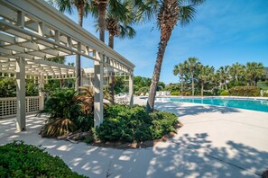 A covered outdoor area with a pool, palm trees, and lounge chairs.