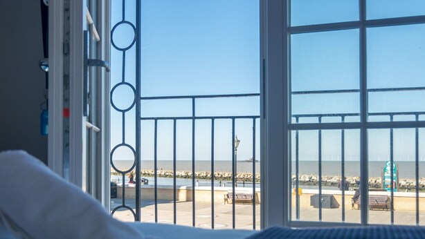 A hotel room with a large window overlooking a beach and promenade.