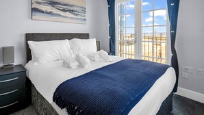 A hotel room with a large bed, a painting on the wall, and a view of the beach through the window.
