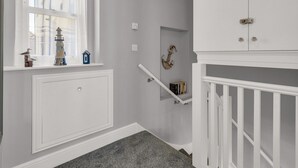 A hallway with a window, a small shelf with decorative items, a white door, and a staircase.