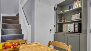 A dining area with a wooden table and chairs, a fruit basket, a grey kitchen with a microwave, and a staircase. - Cute and cosy home in the centre of Canterbury. - Pass the Keys (Canterbury)