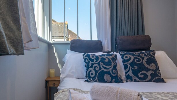 A neatly made bed with white and blue patterned pillows, a folded white towel, and a bedside table with a candle. - Cute and cosy home in the centre of Canterbury. - Pass the Keys (Canterbury)