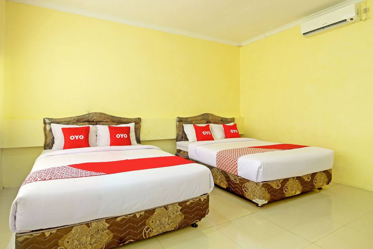 Two single beds with wooden headboards, white bedding, and red pillows with 'OYO' branding.