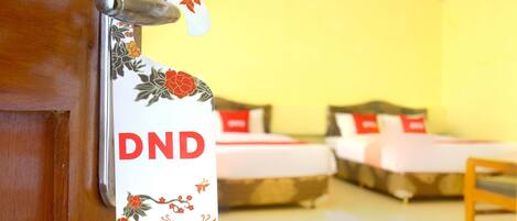 A hotel room with two beds, a wooden door, and a sign with 'DND' written on it.
