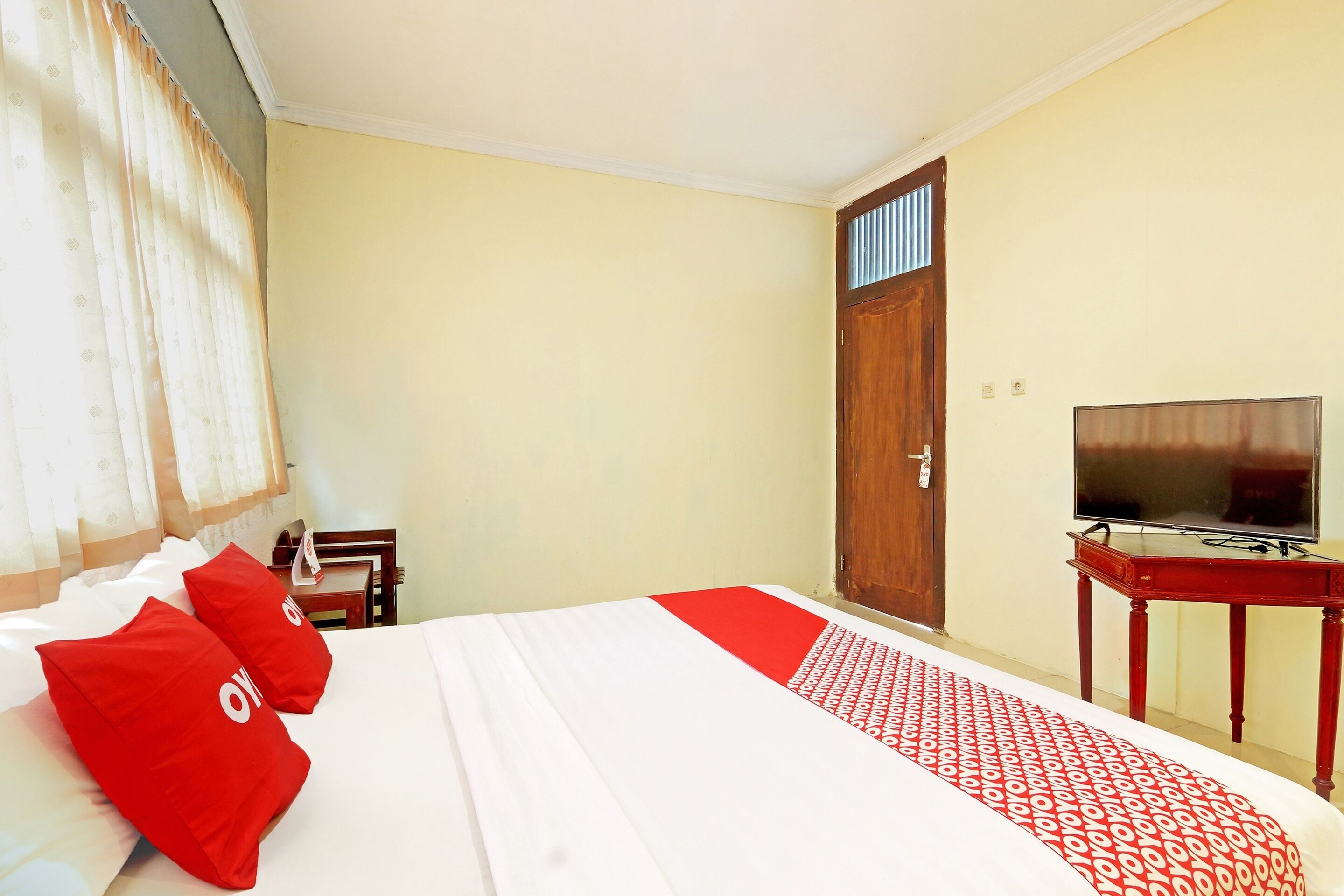 A hotel room with a bed, a TV on a wooden table, and a door with a window.