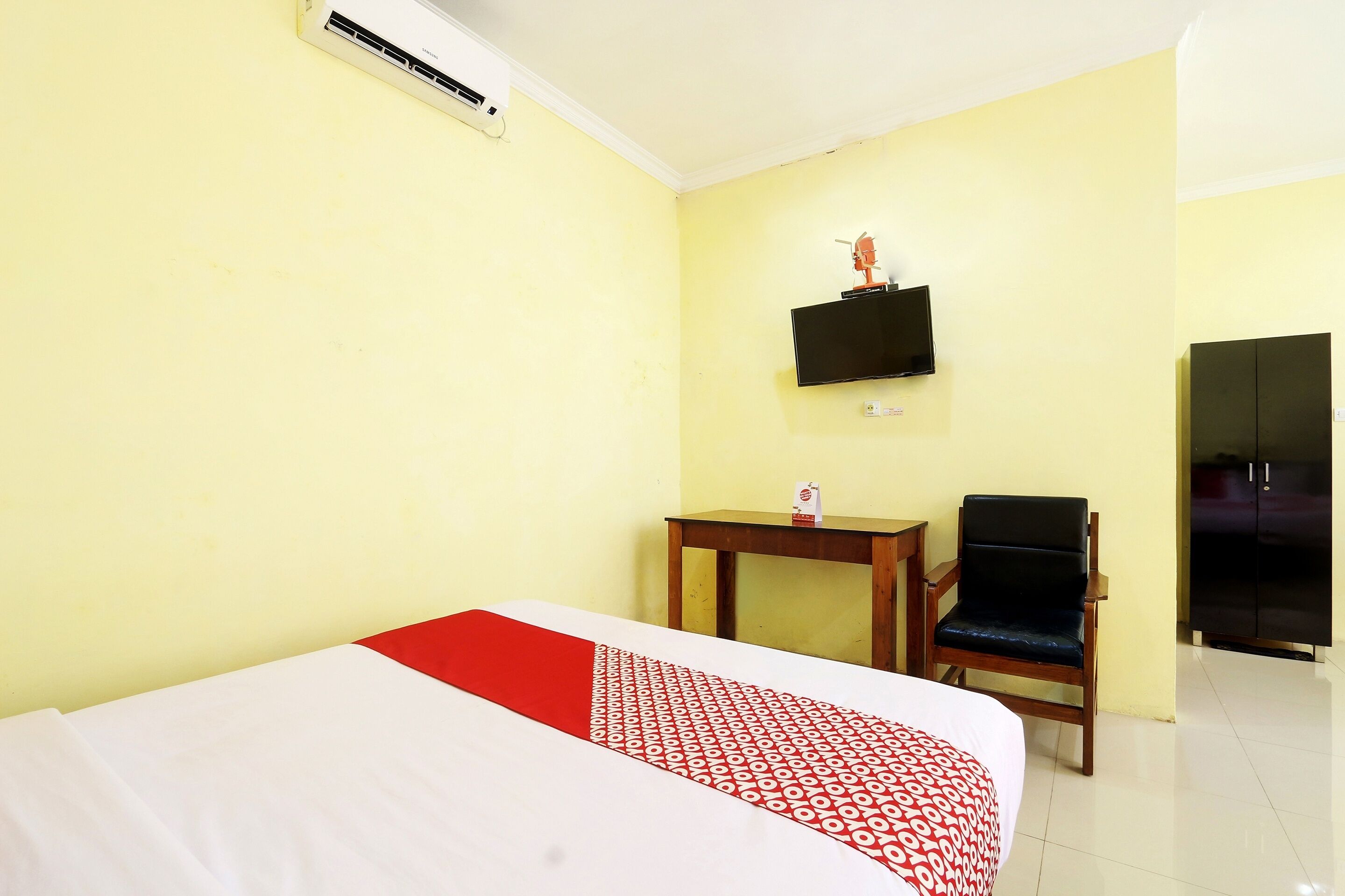 A hotel room with a bed, a television mounted on the wall, a small table, a chair, and a wardrobe.