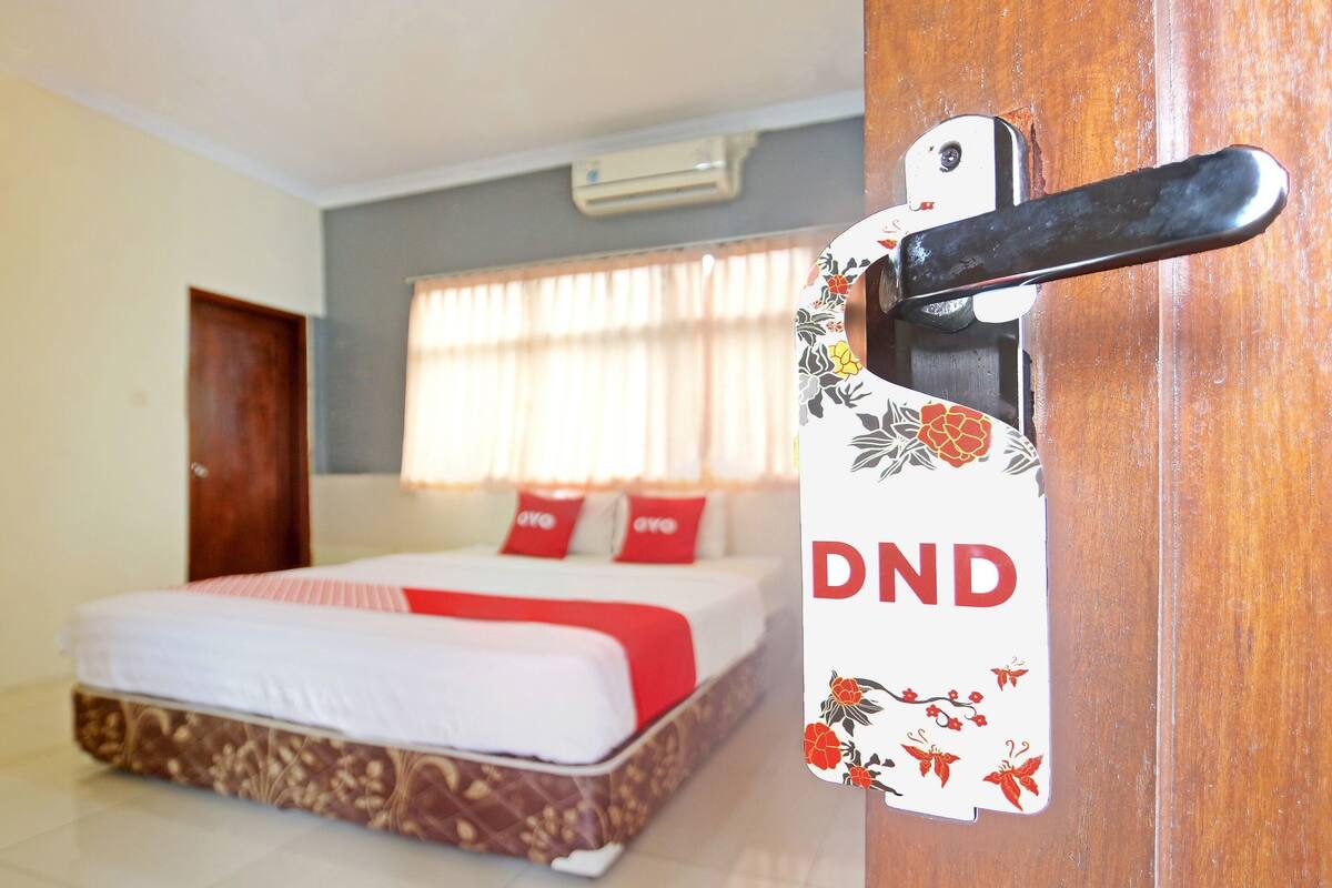 A hotel room with a bed, a wooden door, and a sign with "DND" on it.
