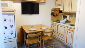 A compact kitchen with wooden cabinets, a microwave, a television, and a dining table with chairs. - Cozy studio in village center - 4 guests (Les Contamines-Montjoie)