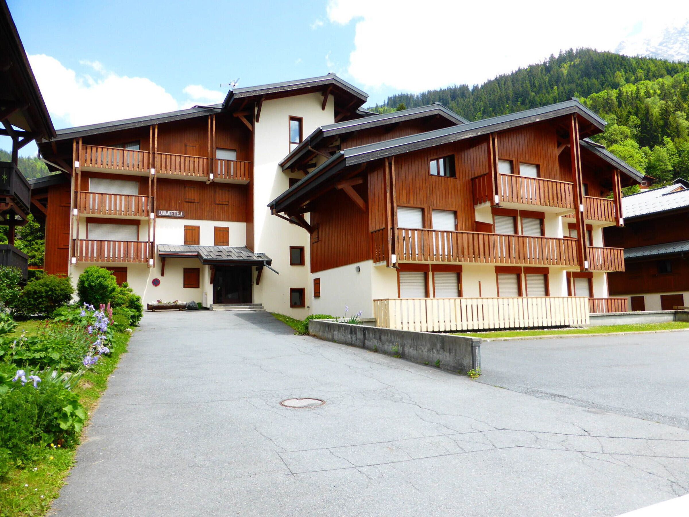 A multi-story building with balconies, a central entrance, and a surrounding garden.