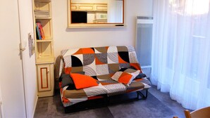 A living room with a sofa, a bookshelf, a mirror, and a window with curtains. - Cozy studio in village center - 4 guests (Les Contamines-Montjoie)
