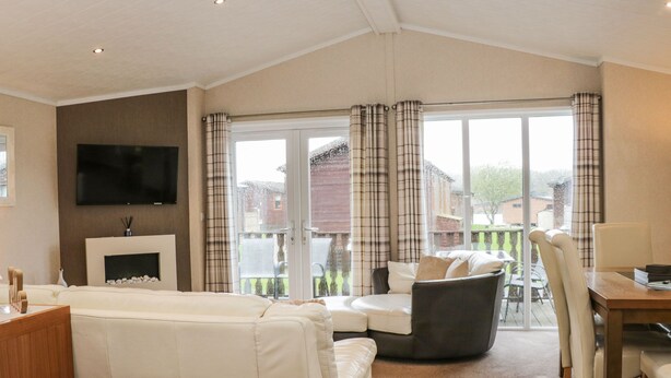 A spacious living room with a large sofa, a dining table with chairs, a flat-screen TV mounted on the wall, and a fireplace.