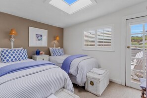 A bedroom with two beds, a skylight, a window with blinds, and a view of outdoor chairs. - Bodega Bay• Beach Retreat • Easy Walk to Sand-Surf-Fun–Fisherman’s Cottage (Bodega Bay)