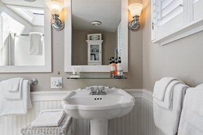 A bathroom with a pedestal sink, two wall-mounted lights, a mirror, and a glass shelf with toiletries.