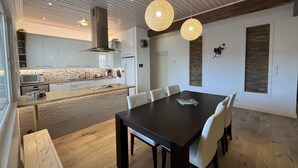 Een moderne keuken met witte kasten, een houten aanrechtblad en een ingebouwde magnetron. Er is een eethoek met een donker houten tafel en witte stoelen.