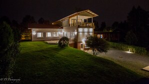 Een modern huis met twee verdiepingen, een balkon, grote ramen en een goed verlichte gevel 's nachts.