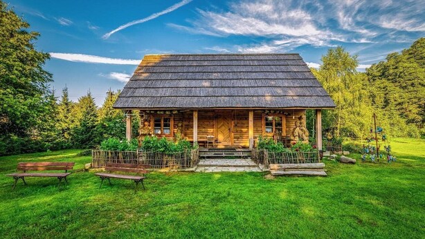 A wooden cabin with a thatched roof, surrounded by a lush green lawn and trees. - Large, atmospheric cottage in the countryside (Belczna)