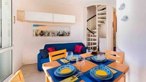 A dining area with a wooden table set for two, blue plates, and a blue sofa with red cushions. - Apartment with swimming pool "Tivoli" (Bibione)