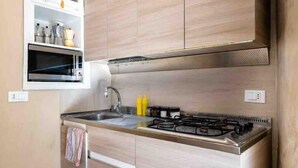 A modern kitchen with a built-in oven, stainless steel stove, and wooden cabinetry. - Apartment with swimming pool "Tivoli" (Bibione)