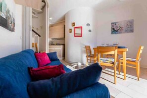 Un soggiorno con divano blu, cuscini rossi, un tavolo da pranzo con sedie e una cucina sullo sfondo.