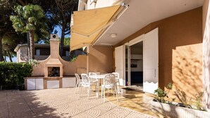 An outdoor patio with a table and chairs, a barbecue grill, and a covered seating area. - Apartment with swimming pool "Tivoli" (Bibione)