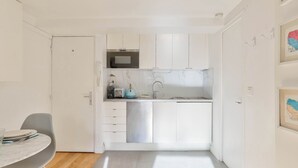 Een kleine keuken met witte kasten, een magnetron en een spoelbak. Er is een zithoek met een tafel en stoelen.
