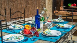 An outdoor dining table set with plates, cutlery, and a bottle of wine, surrounded by chairs and a stone wall. - House in Puerto Pollensa Villa Pintor with pool (Puerto Pollensa)