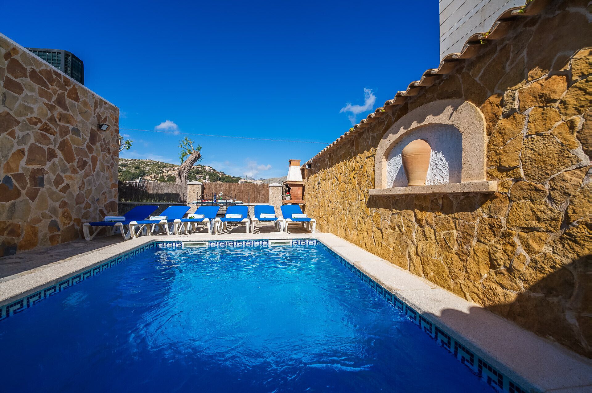 A swimming pool with blue tiles, surrounded by stone walls and blue lounge chairs.
