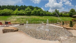 A water feature with jets, surrounded by a paved area with seating and a fence. - SAVE! 2 Min to Pkwy! Luxury Apt Best Price (Sevierville)