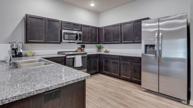 A modern kitchen with dark wood cabinets, stainless steel appliances, granite countertops, and a light wood floor. - SAVE! 2 Min to Pkwy! Luxury Apt Best Price (Sevierville)