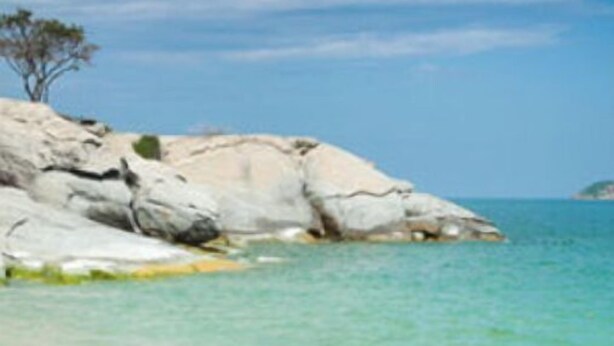 Ein Strand mit klarem türkisblauem Wasser, weißem Sandstrand und Felsformationen.
