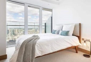 Relax in a spacious bedroom with a large bed and floor-to-ceiling windows offering a city view.