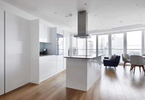 Experience a sleek, modern space with a central island kitchen, seating area, and large windows offering a city view.