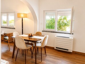 A dining area with a table, chairs, a lamp, and a window with a view of greenery.
