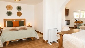 Ein Zimmer mit einem Bett, einem Tisch, einem Stuhl, einem Heizkörper und einer Küchenzeile.