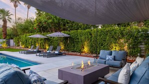A poolside area with lounge chairs, a fire pit, and umbrellas.