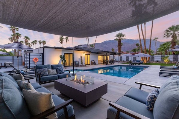 Zona junto a la piscina con mobiliario exterior, una chimenea y vistas a las montañas.