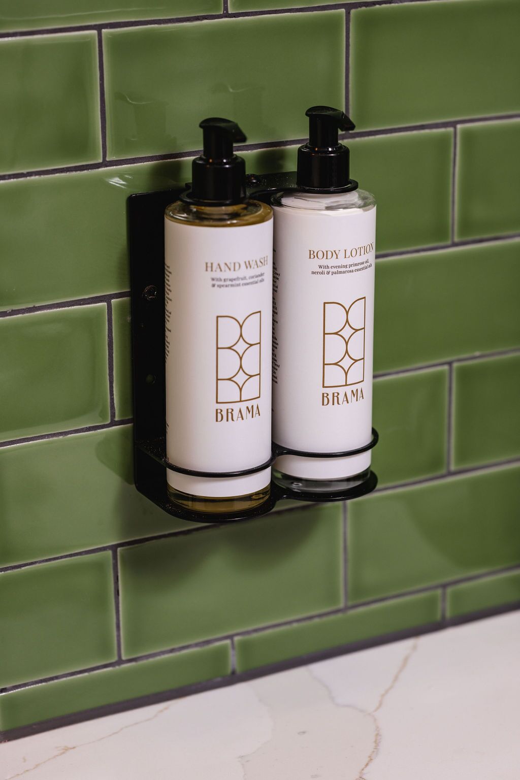 Two Brama hand wash and body lotion bottles mounted on a green tiled wall.