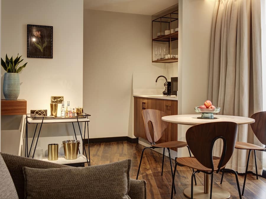 Ein modernes Wohnzimmer mit einer Couch, einem Couchtisch und einem Essbereich mit Tisch und Stühlen. Es gibt eine Küchenzeile mit Spüle und Schränken.