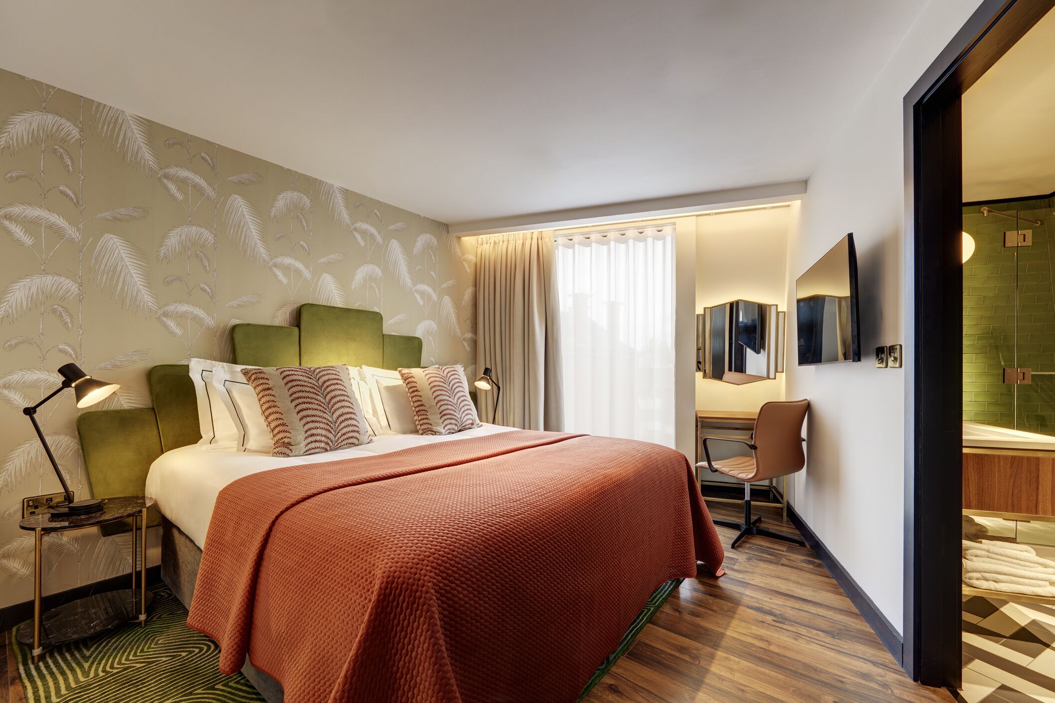 Habitación de hotel con cama, escritorio, silla, espejo y baño con ducha e inodoro.