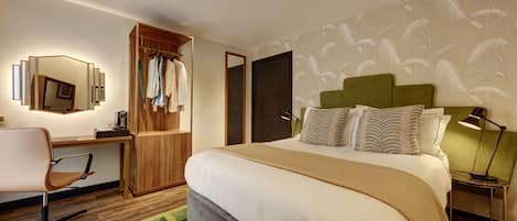 A hotel room with a bed, a desk, a chair, a wardrobe, and a mirror.