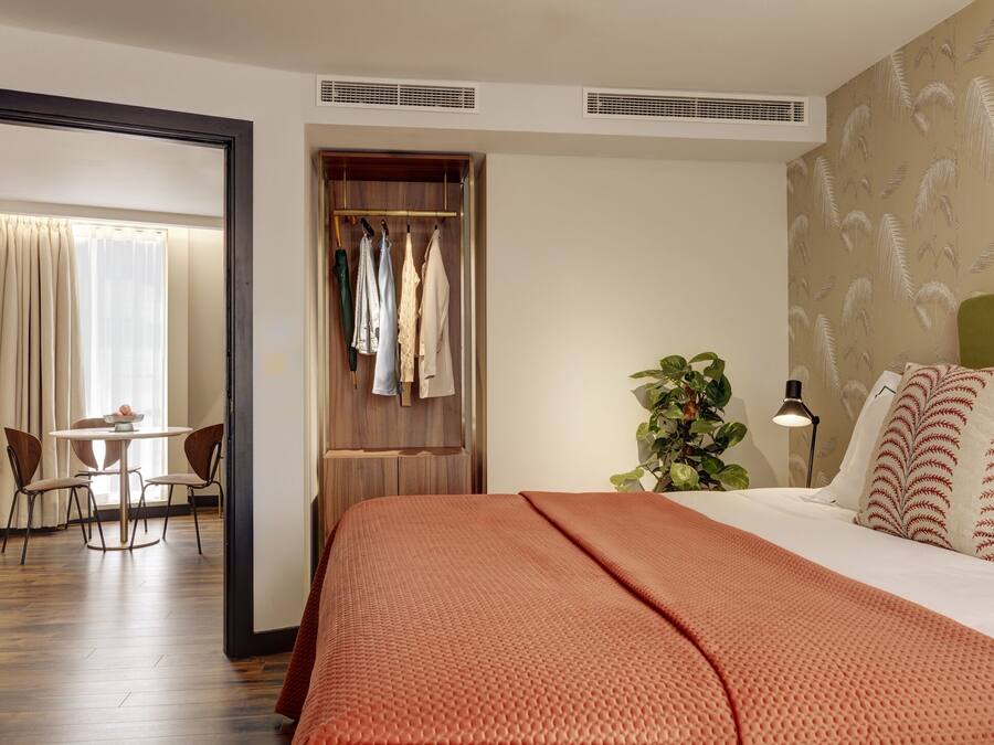 Una habitación de hotel con cama, escritorio, silla, armario y una planta.