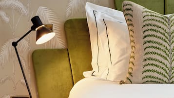 Una cama bien hecha con cabecera verde, una lámpara de noche y almohadas estampadas.