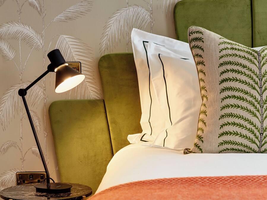 Una cama bien hecha con cabecera verde, una lámpara de noche y almohadas estampadas.