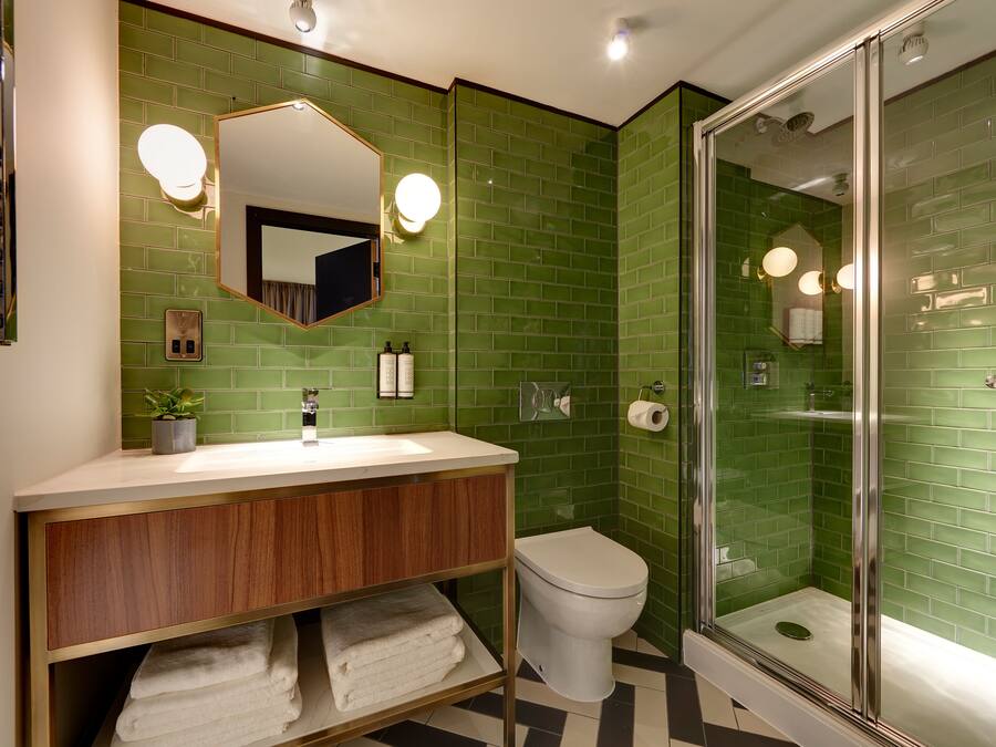 Ein Badezimmer mit grünen Fliesenwänden, einem weißen Waschbecken mit Holzschrank, einer weißen Toilette und einer Duschkabine.