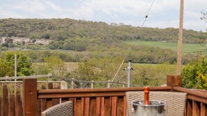 A wooden deck with a table and chairs, overlooking a green landscape with hills and a distant village. - Dulas (Llandudno Junction)