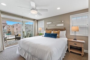 A bedroom with a large bed, a ceiling fan, a nightstand with a lamp, and a view of the outside. - Pacific Surf | 3BD Steps from Mission Beach (San Diego)