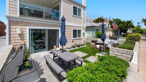 A two-story house with a patio area featuring a barbecue grill, outdoor seating, and a small garden. - Pacific Surf  in Mission Beach | Steps to the Sand (San Diego)