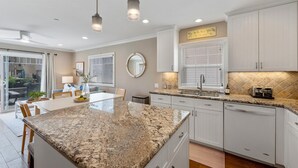 A modern kitchen with granite countertops, white cabinetry, and a dining area with a table and chairs. - Pacific Surf  in Mission Beach | Steps to the Sand (San Diego)